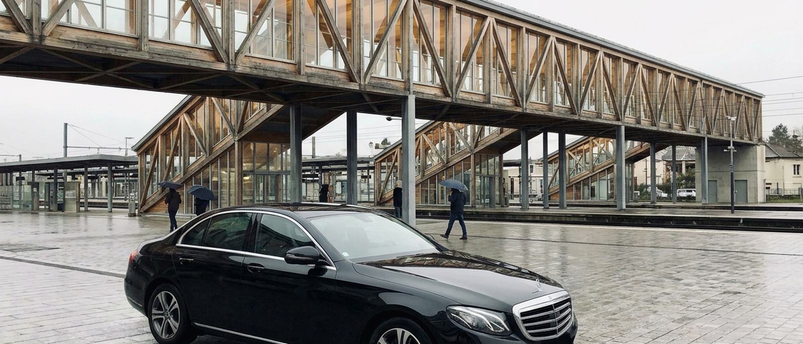Berline noire devant une gare contemporaine à charpente de bois lamellé-collé