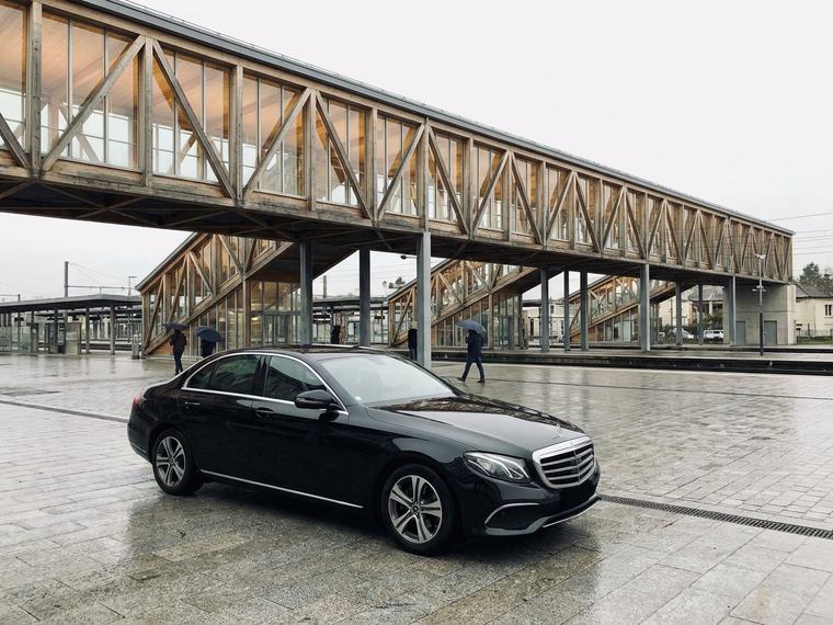 Berline noire devant une gare contemporaine à charpente de bois lamellé-collé