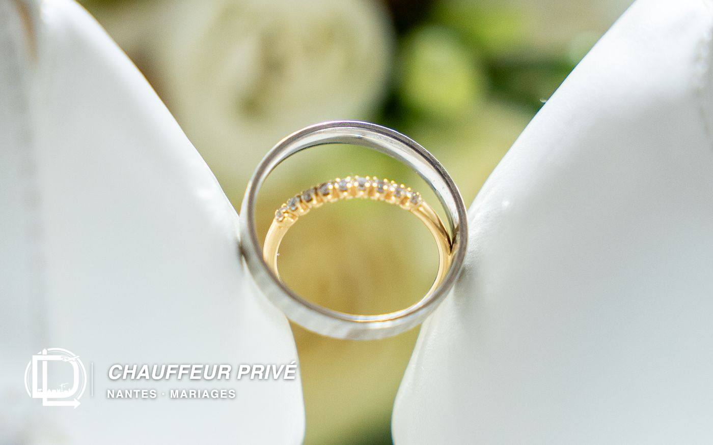 Deux alliances, une en or blanc et une en or jaune sertie de diamants, posées sur un bouquet de roses blanches