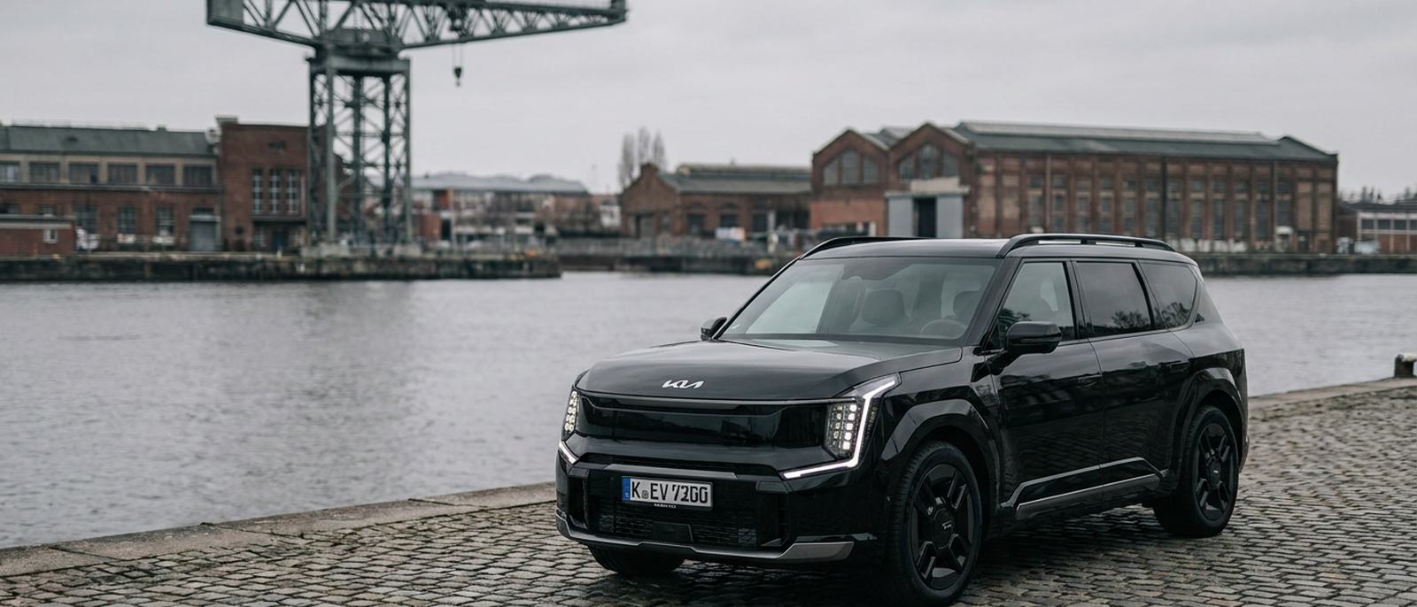 Voiture avec chauffeur sur un quai en bord de fleuve, devant une grue portuaire
