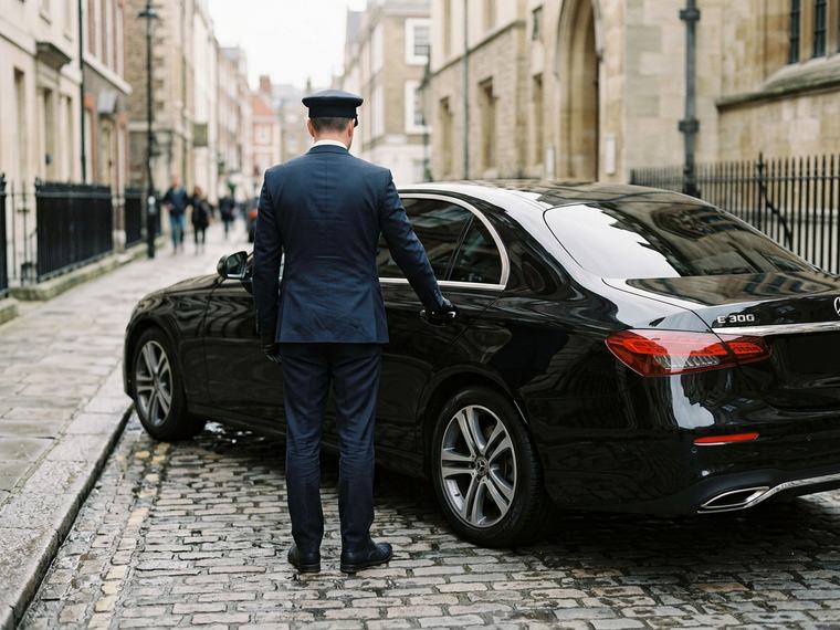 Chauffeur ouvrant la portière arrière d’une berline noire dans une rue calme